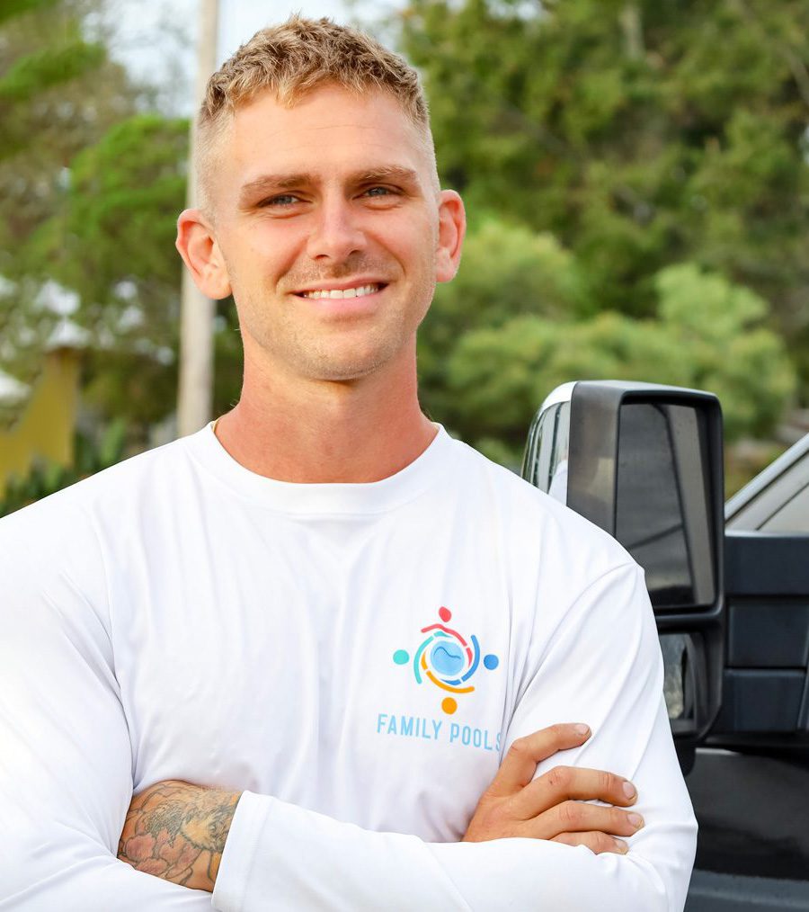 Max Lautenschlager, owner of Florida Family Pools, smiling in a white long-sleeve shirt with the company logo, standing confidently in front of a vehicle.