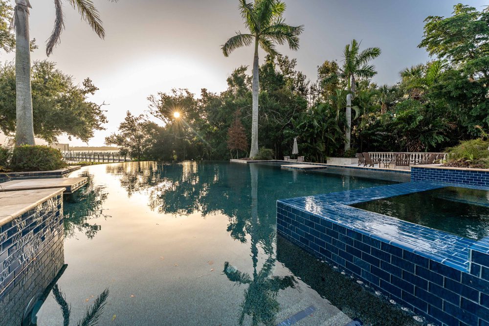 Luxurious custom pool with blue tile accents, surrounded by tropical landscaping and palm trees, reflecting a serene sunset, showcasing Family Pools' expertise in creating personalized outdoor spaces.