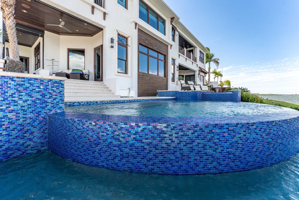 Luxury infinity pool with mosaic tiles, adjacent to a modern home, showcasing outdoor living space and serene water features.