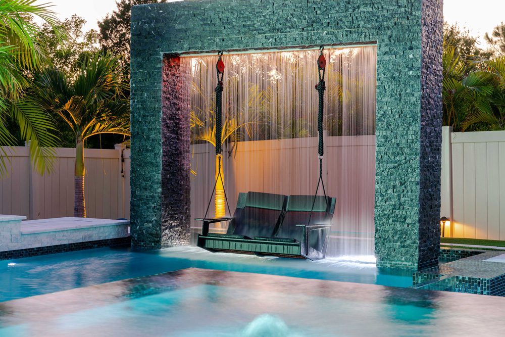 Poolside swing with water feature and tropical landscaping, showcasing custom pool design by Florida Family Pools.