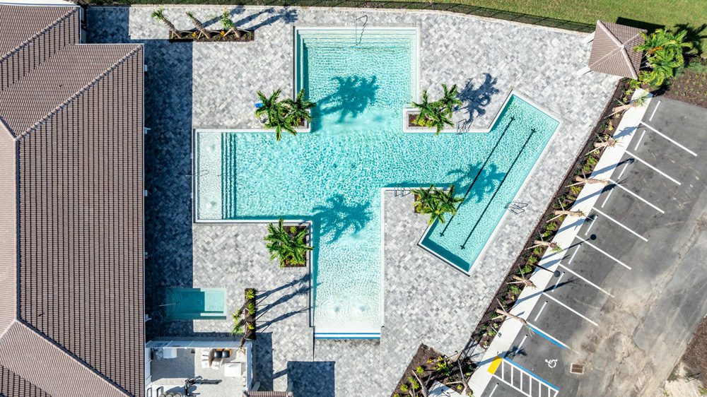 Aerial view of a modern pool design featuring an intricate layout with multiple connected sections, surrounded by palm trees and paved areas, showcasing Florida Family Pools' custom pool construction expertise.