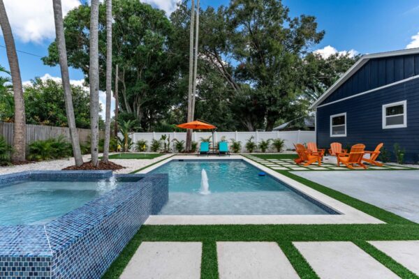 Resort-style outdoor retreat featuring a sparkling pool, spa with mosaic tile, vibrant orange lounge chairs, and palm trees, designed to enhance guest experience in vacation rentals.
