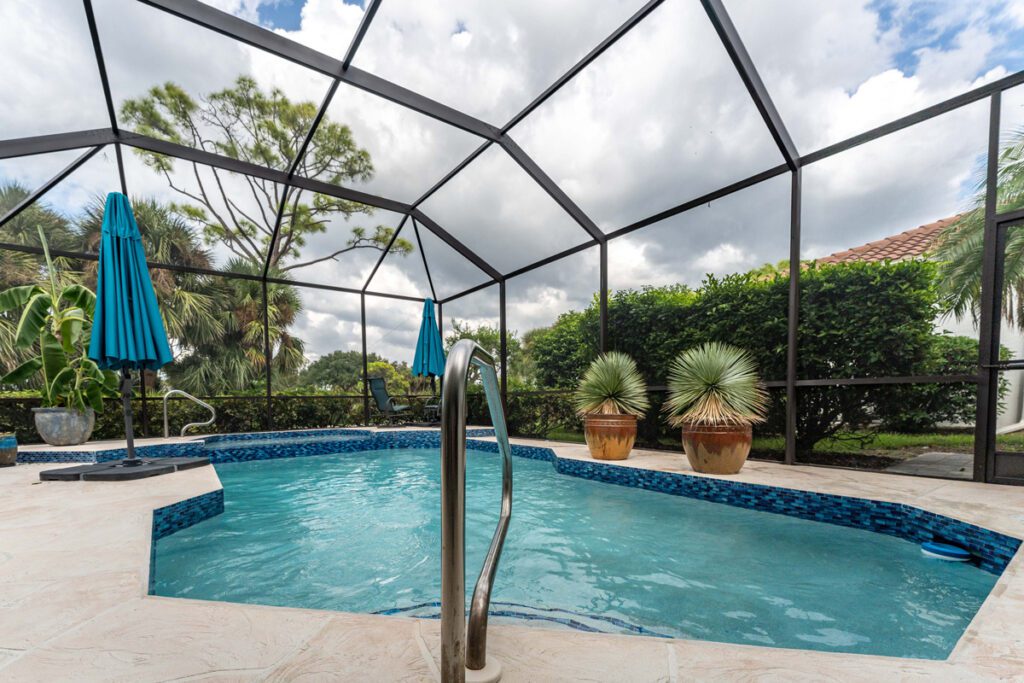 Custom pool design featuring a blue-tiled edge, surrounded by lush greenery and two blue umbrellas, under a screened enclosure, showcasing Florida Family Pools' craftsmanship.