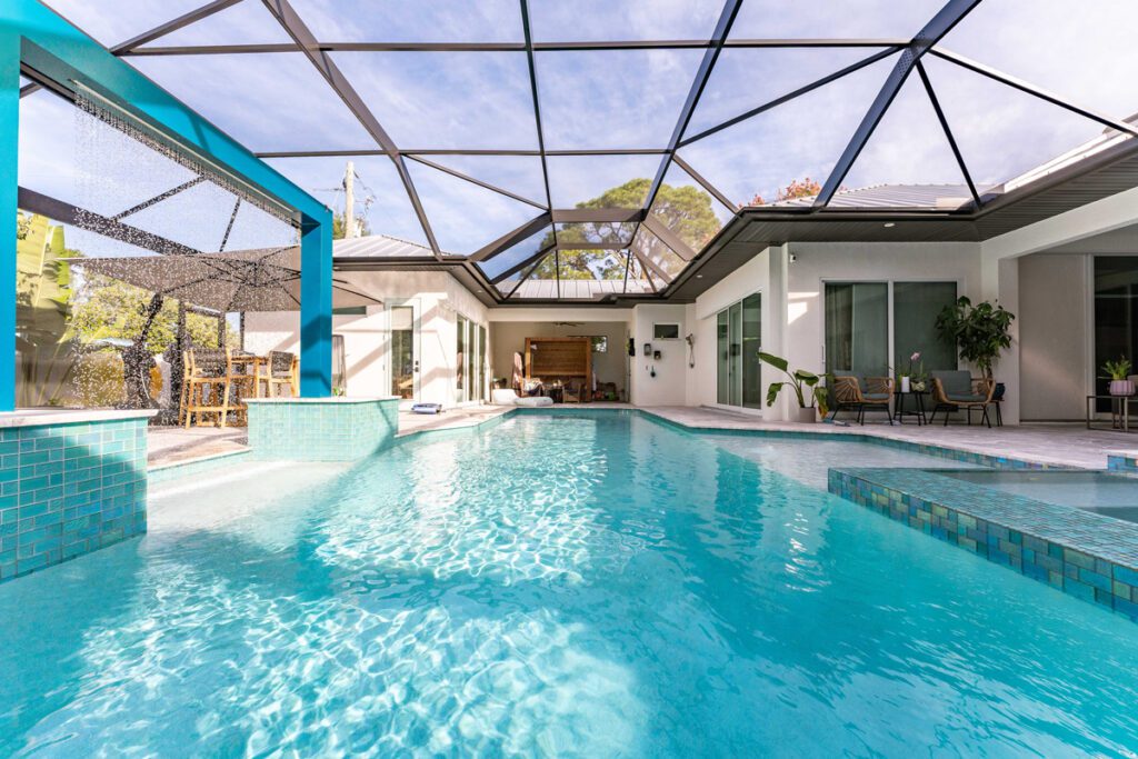 Modern pool design with turquoise tiles, covered patio area, and outdoor seating, showcasing the elegant pool construction by Florida Family Pools.