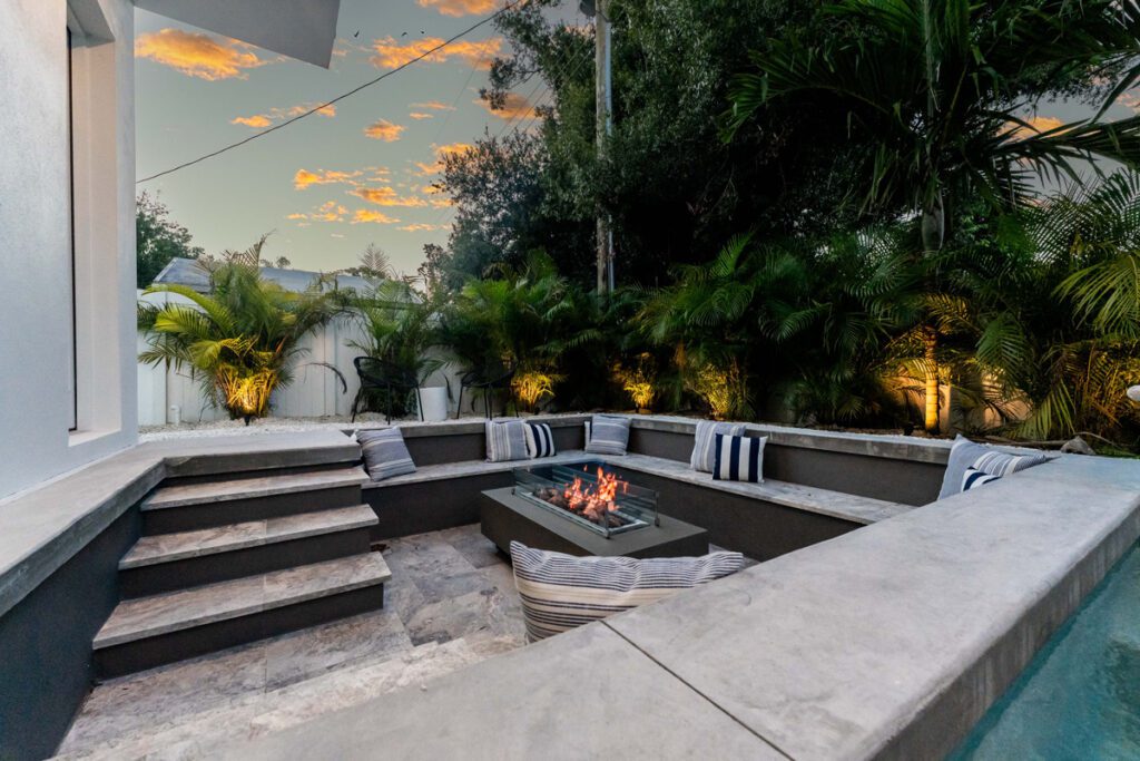 Modern outdoor seating area with fire pit, surrounded by lush greenery, showcasing a tranquil evening ambiance, designed by Florida Family Pools.