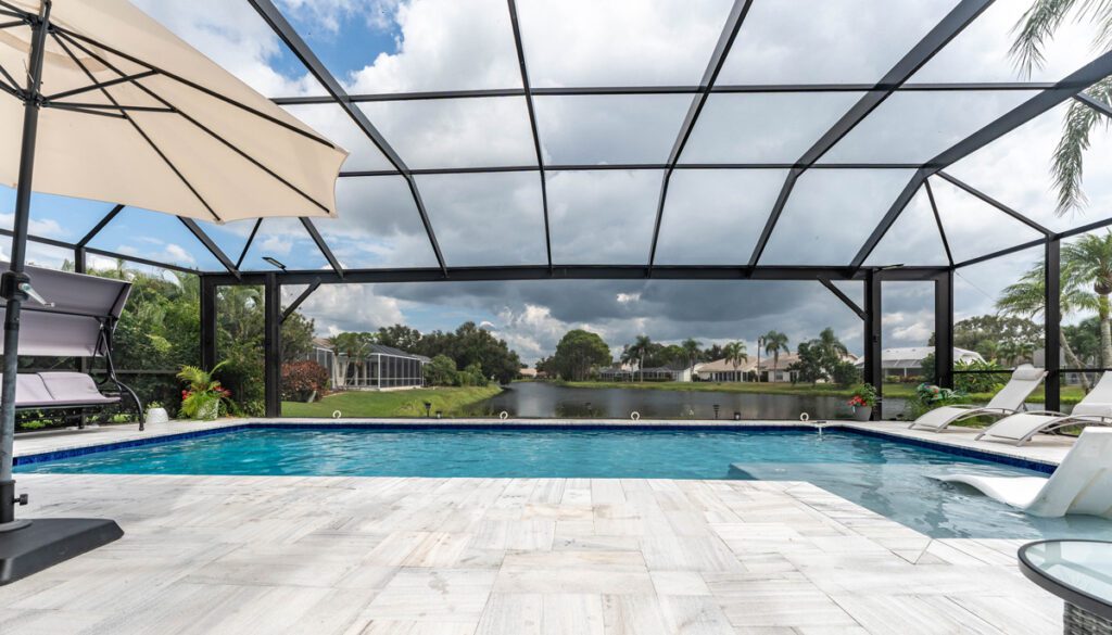 Modern pool with a screened enclosure, lounge chairs, and umbrella overlooking a serene waterway, showcasing Florida Family Pools' design expertise.