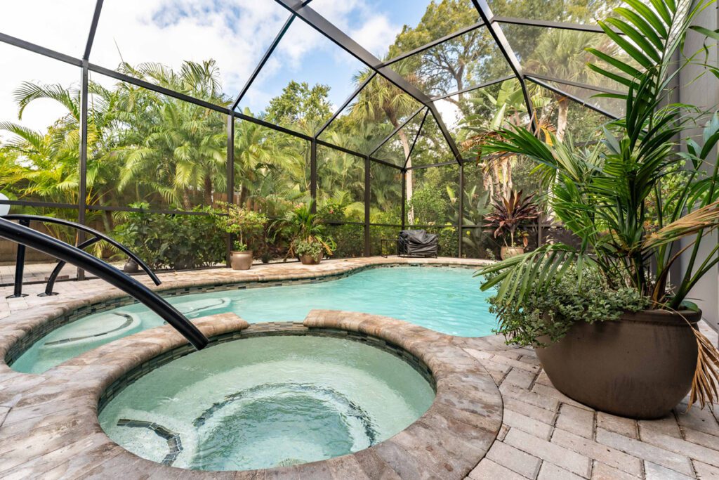 Custom pool with integrated spa and tropical landscaping, enclosed by a screened patio, showcasing Florida Family Pools' design expertise.