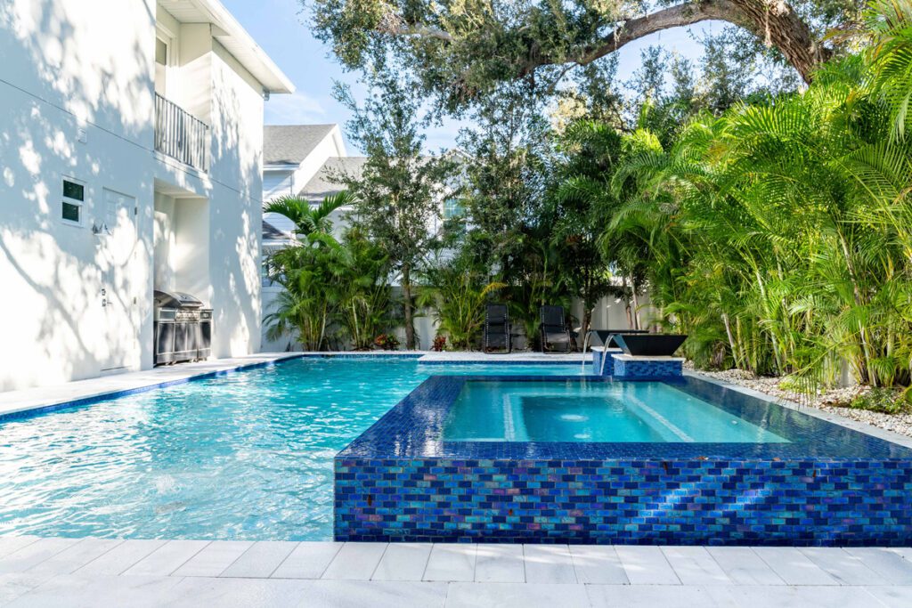 Custom swimming pool with a spa, surrounded by lush greenery and modern outdoor furniture, showcasing Florida Family Pools' design expertise.