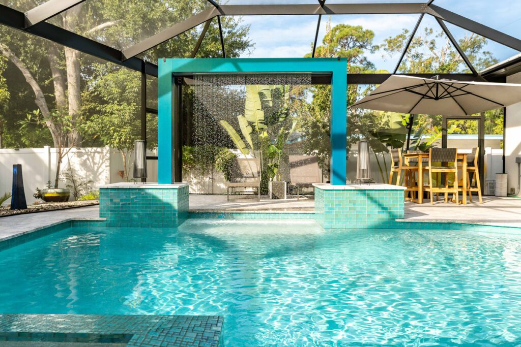 Custom pool design featuring a turquoise water feature, surrounded by a screened enclosure, patio furniture, and lush greenery, showcasing Florida Family Pools' expertise in pool construction.